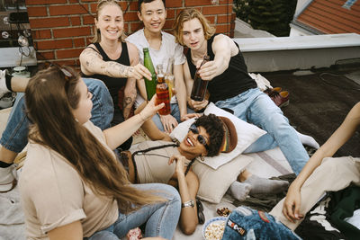 Happy male and female toasting beer bottles enjoying on rooftop