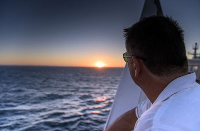 Close-up of man sailing in sea against sky during sunset