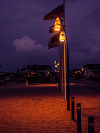 Illuminated street by sea against sky at night