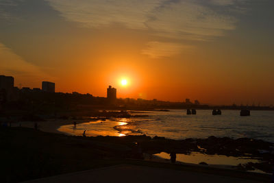 Silhouette buildings by sea against sky during sunset