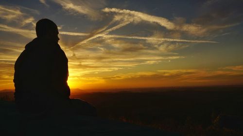 Silhouette man standing on cliff at sunset