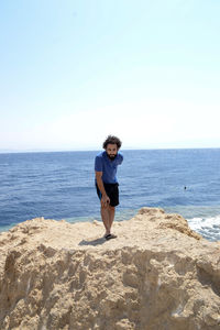 Portrait of man standing on rock at beach against sky