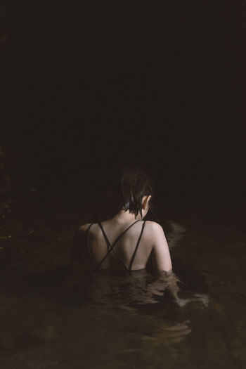 REAR VIEW OF WOMAN SITTING ON SAND AT NIGHT