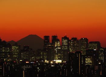 Illuminated buildings against orange sky during sunset