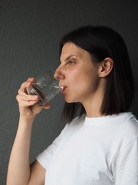 Young woman drinking water against black background