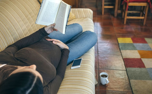 High angle view of woman reading book while lying on sofa at home