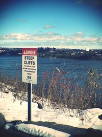 Information sign by lake against sky during winter