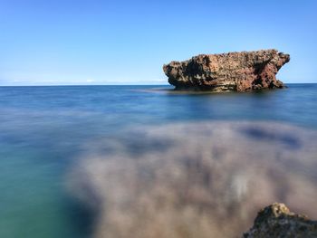 Rock formation in sea against clear blue sky