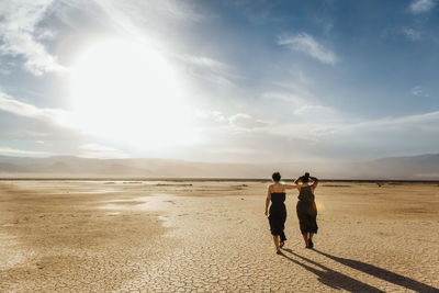 Friends walking on desert against sky during sunny day