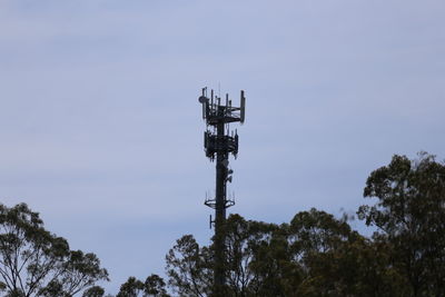 Low angle view of communications tower above trees against sky