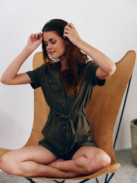 Portrait of young woman sitting on chair against white background