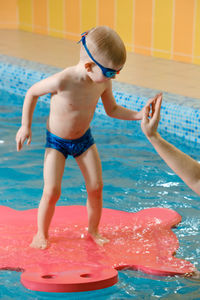 Toddler child learning to dive in indoor swimming pool with teacher. standing on side, balancing and