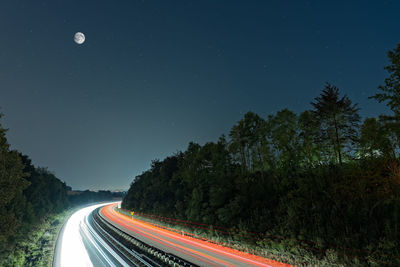 Light trails on road amidst trees at night