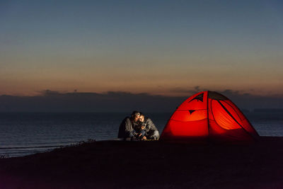 Romantic couple camping on the beach, using smartphone