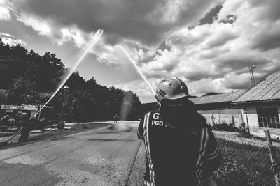 Firefighter spraying water on road against cloudy sky