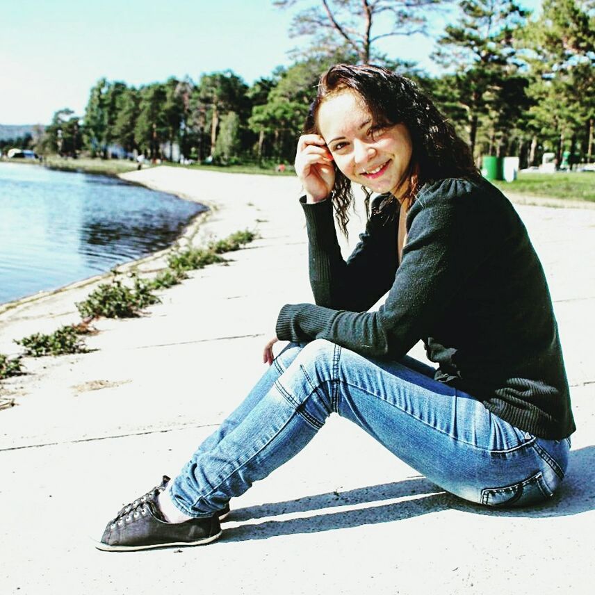 PORTRAIT OF YOUNG WOMAN SITTING ON TREE TRUNK