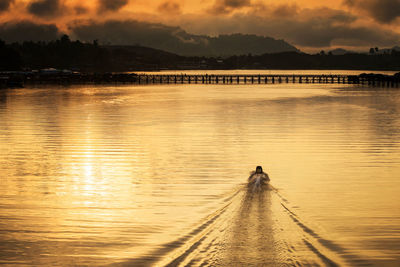 Silhouette man sailing boat in lake to wooden bridge against sky during sunrise