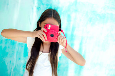 Teenage girl photographing with instant camera against wall