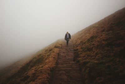 Hiker walking on mountain against sky during foggy weather