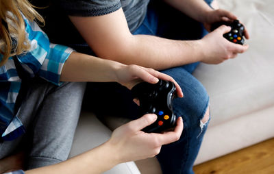 Midsection of friends playing video game on sofa at home