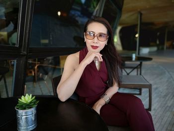 Portrait of fashionable woman wearing sunglasses sitting by window