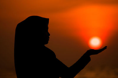 Silhouette man holding orange sun against sky during sunset