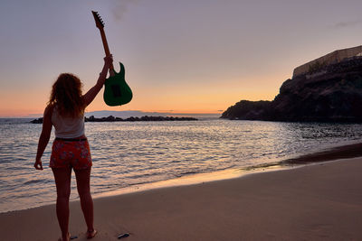 Rear view of woman standing at beach during sunset