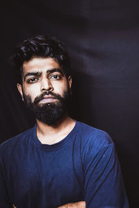 Portrait of young man standing against black background