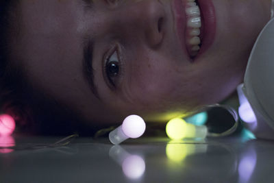 Close-up portrait of young woman lying down on floor with illuminated light