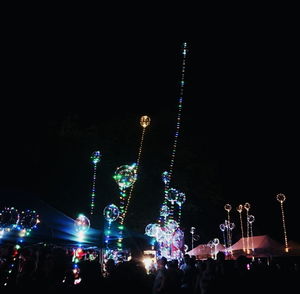 People on illuminated street lights against sky at night