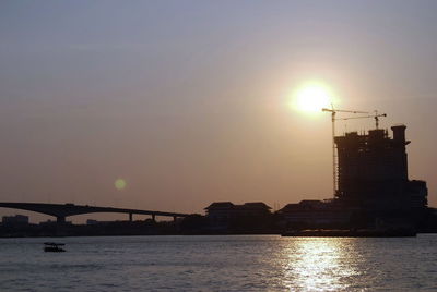 Silhouette bridge over sea against sky during sunset