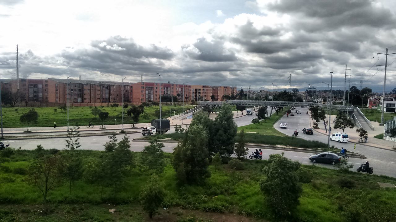 building exterior, sky, architecture, built structure, cloud - sky, transportation, city, cloudy, tree, high angle view, mode of transport, car, cloud, connection, residential building, land vehicle, outdoors, road, day, residential structure