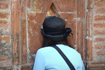 Rear view of woman peeking through hole in wall