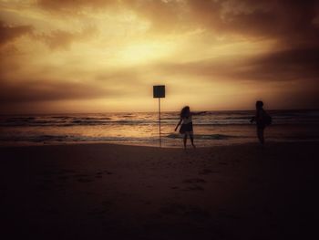 Silhouette people on beach against sky during sunset