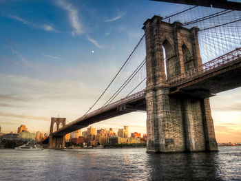 Suspension bridge over river against cloudy sky