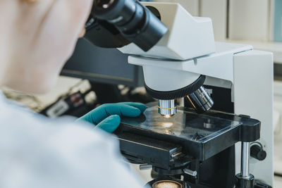 Young woman analyzing human brain microscope slide under microscope while sitting at laboratory