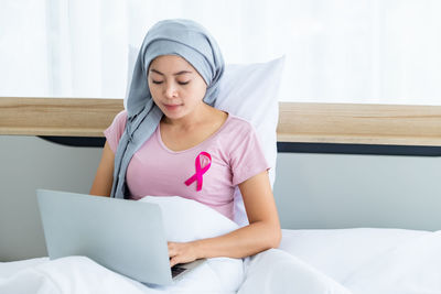 Young woman using phone while sitting on bed