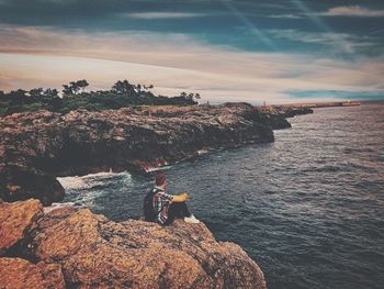 People standing on rock by sea against sky