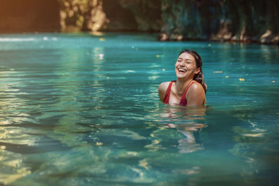 Young latina woman standing, laughing a lot, in blue green waters of rio blanco in costa rica