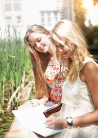 Smiling woman looking at friend writing in book at park