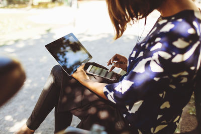 Side view of businesswoman using smart phone and digital tablet while sitting on bench