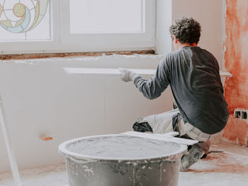 A young caucasian plasterer plasters the walls and checks them for evenness with a large wooden rule