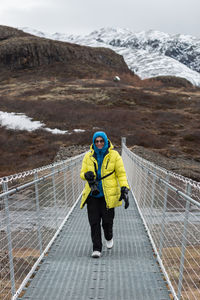 A smiling woman photographer walking in scenic iceland over a footbridge