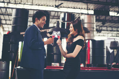Side view of smiling couple toasting red wineglasses while standing in bar
