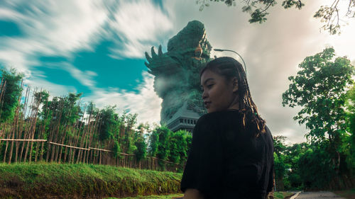 Side view of young woman standing against trees