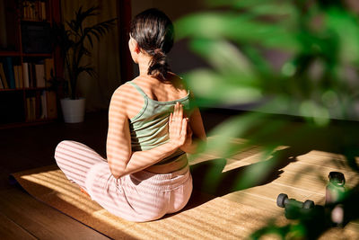 Woman doing gomukhasana or cow face pose sitting in lotus pose on yoga mat. practicing yoga at home.