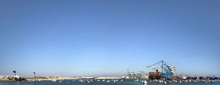 Cranes at harbor against clear blue sky