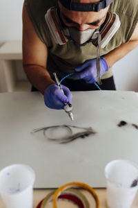 Close up of airbrush painter with mask drawing an eye on a paper.