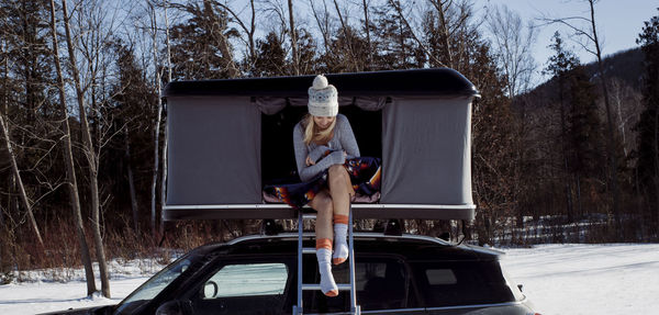 Full length of woman sitting in roof tent on car during winter