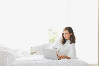 Young woman using mobile phone while sitting on bed